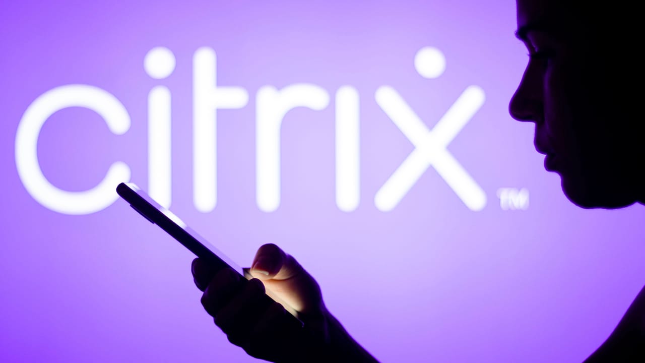 Citrix Systems logo is seen in the background of a silhouetted woman holding a mobile phone